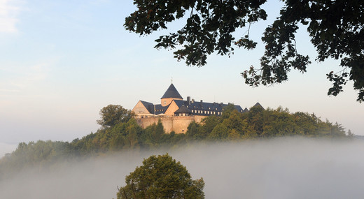 Das Schloss Waldeck aus der Ferne; Es ragt auf einem Berg, der von morgendlichen Nebel umhüllt ist